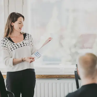 Nainen seisoo paperi kädessään ja puhuu muille ihmisille.