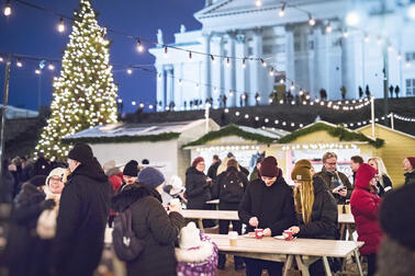 Ihmisiä torikojujen edessä Senaatintorilla. Taustalla Tuomiokirkko ja joulukuusi.