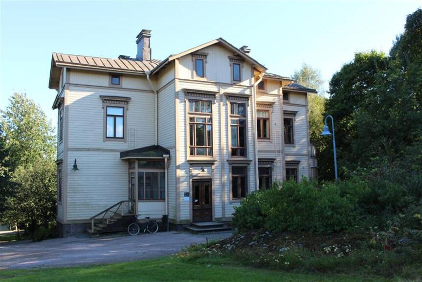 Light-coloured three-storey wooden villa surrounded by verdant trees.