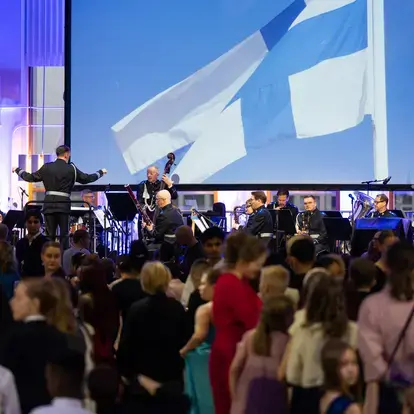 Lapsia tanssimassa, Suomen lippu ja orkesteri taustalla.