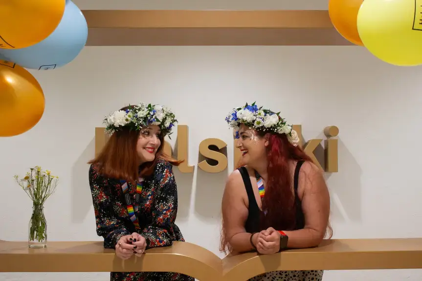 Two smiling women with flowers in their hair at the City Hall's Helsinki logo.