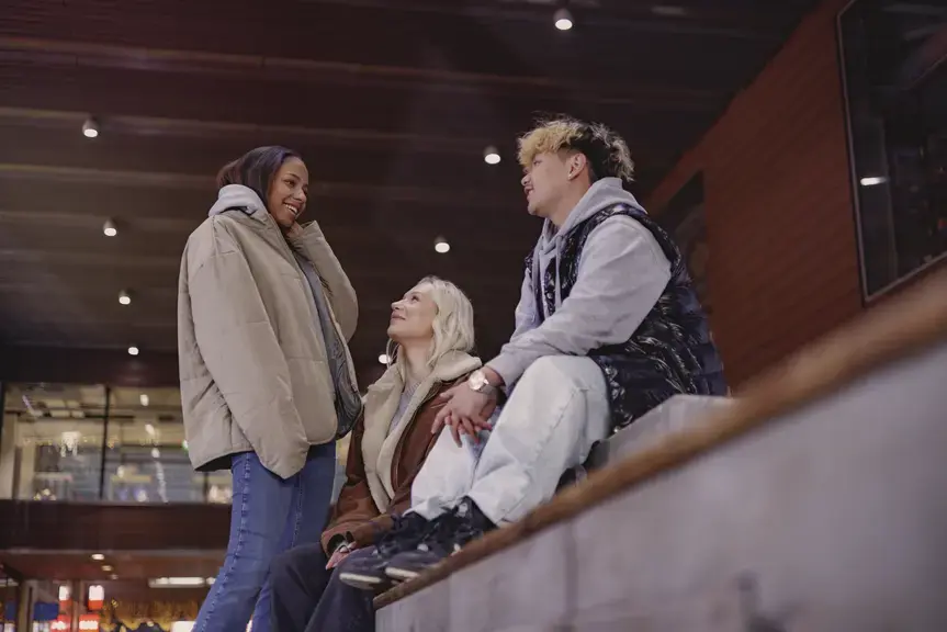 Tre unga personer samtalar på en trappa utomhus.