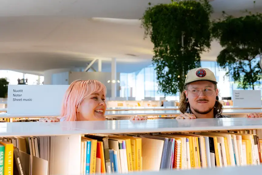 Mies ja nainen katsovat toisiaan kirjaston kirjahyllyjen välissä.