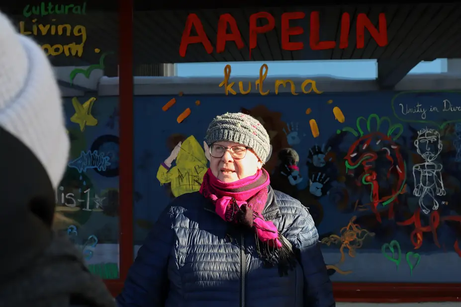 A woman wearing a beret stands in front of a colorful window.