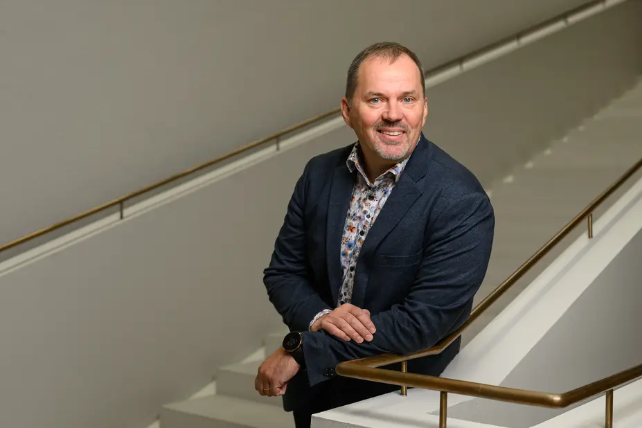 HR Director Petri Lumijärvi leans against the railing of the City Hall staircase and looks at the camera with a smile.