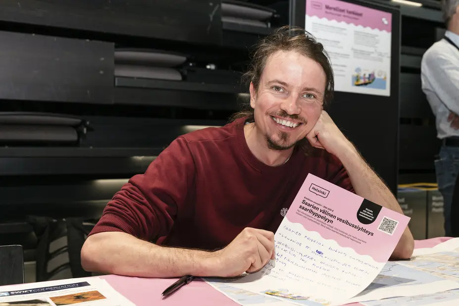 A smiling Ville Saukkonen is holding an OmaStadi proposal form he has filled in.