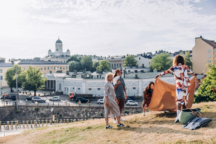 En grupp människor på picknick, med Helsingfors domkyrka i bakgrunden.