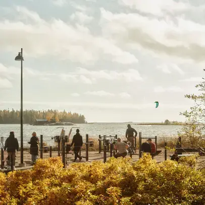 Ihmisiä ulkokuntosalilla meren äärellä tuulisella säällä.
