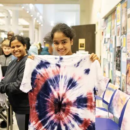A young person holding a tie-dyed t-shirt and smiling. 