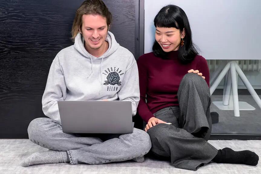 Två personer sitter på golvet och tittar på en bärbar dator.