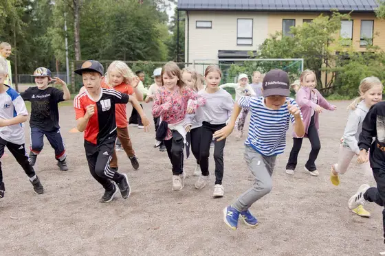 Lapsia juoksee koulun pihalla leikkimässä.
