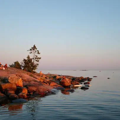 Henkilöitä rantakalliolla ilta-auringossa.