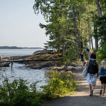 Kävelijöitä rantatiellä, puita ja meri.