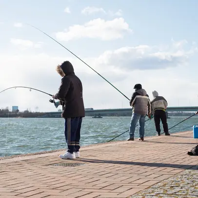 Henkilöitä onkimassa kiviseltä rantakaistaleelta.