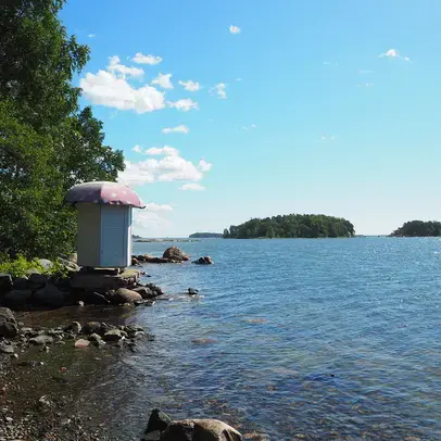 Kivisellä rannalla uimakoppi, meri ja puita.