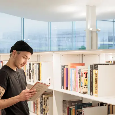 En person tittar på en bok mellan Odes bokhyllor.