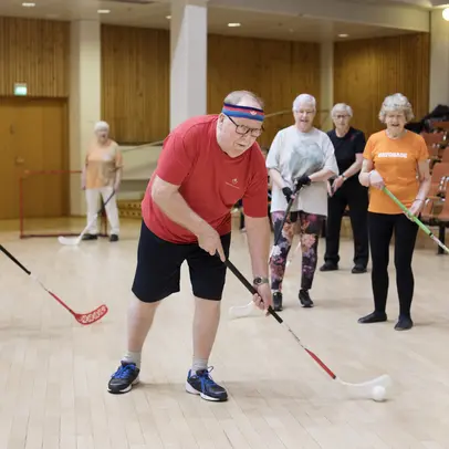 Fem äldre personer spelar innebandy i en idrottshall.