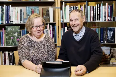 Henkilö opastaa ikääntynyttä tabletin käytössä