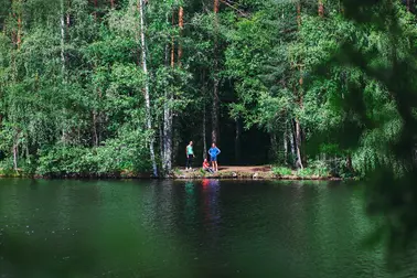 Kolme henkilöä metsän reunala vesistön rannalla.