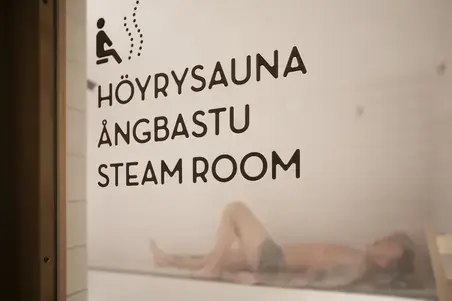 A person lying on the benches is visible through the steam sauna door at Yrjönkatu Swimming Hall.
