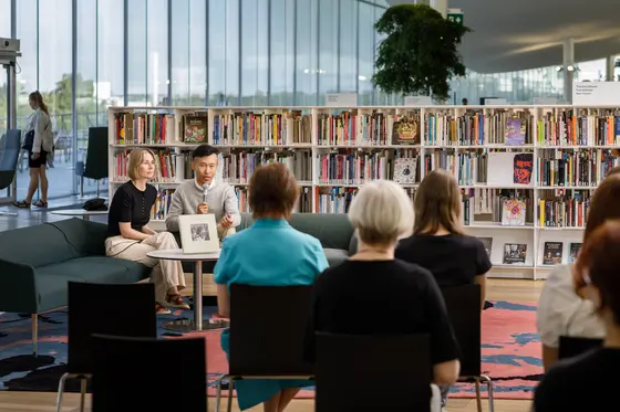 Kirjailija ja haastattelija istuvat sohvalla keskustakirjasto Oodissa ja keskustelevat mikrofoniin yleisön edessä.