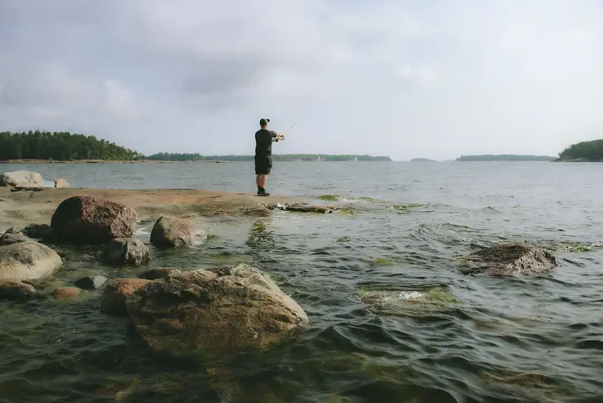 Kalastaja vavan kanssa kallion päällä meren äärellä.