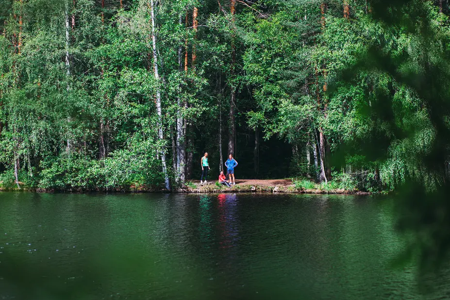 Kolme henkilöä metsän reunala vesistön rannalla.