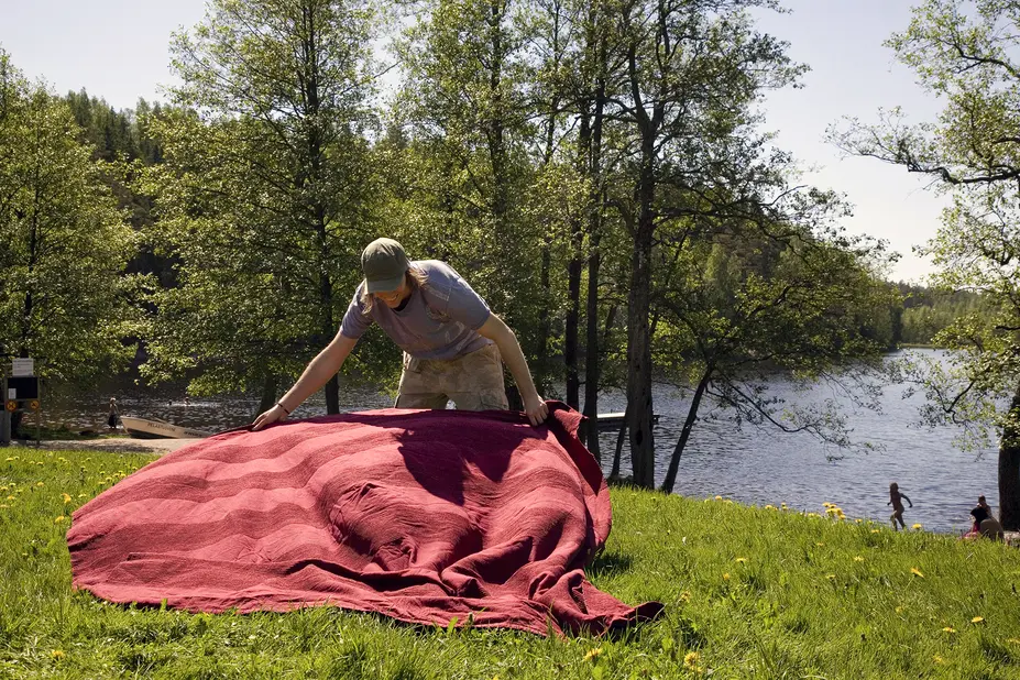 Henkilö levittämässä vilttiä nurmialueelle.