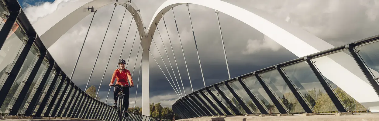 En kvinna cyklar på Aurorabron iförd en orange skjorta.