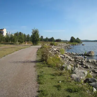 Rannassa kulkee hiekkatie ja taaempana näkyy puita ja rakennuksia.