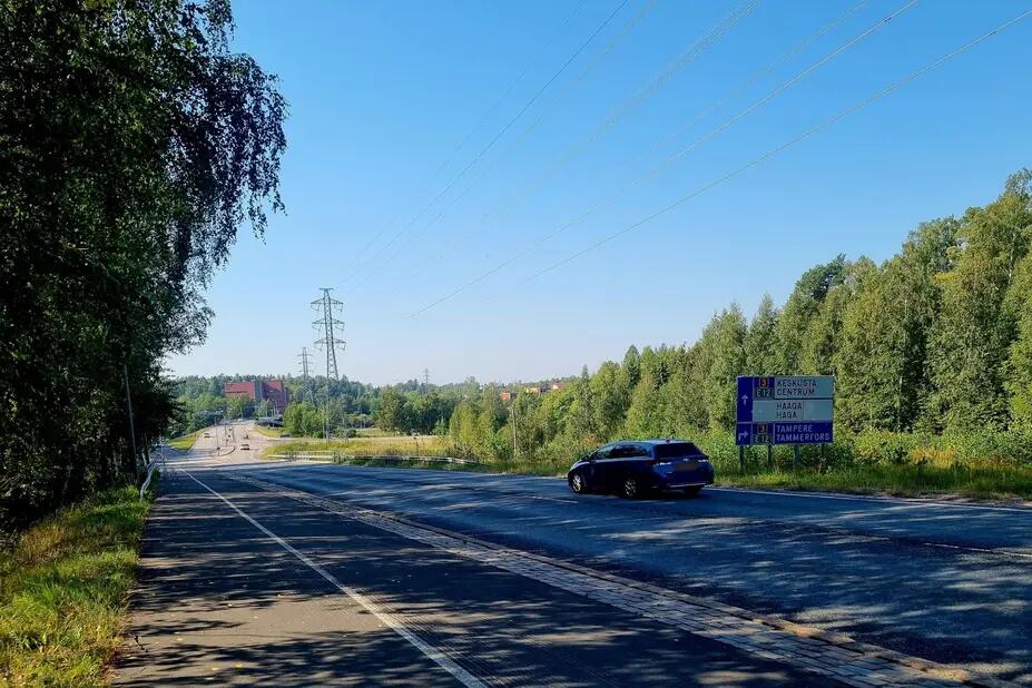 Auto kulkee tiellä, jonka molemmilla puolilla kasvaa metsää.