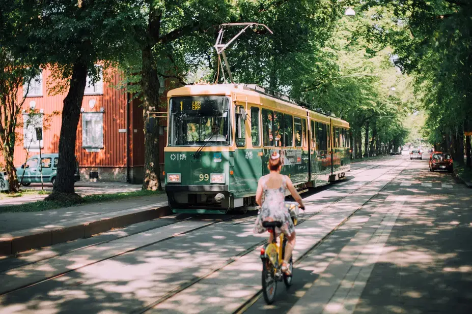 Nainen pyöräilee vehreällä kadulla ja vastaan tulee raitiovaunu.