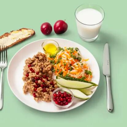 Half a serving of ready-made liver casserole topped with grated salad and cucumber slices, served with fresh lingonberries and a slice of rye bread. A glass of milk to drink and a few cherries for dessert.