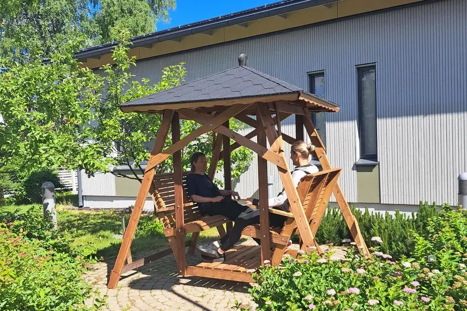 Två personer sitter i en gårdsgunga på en sommargård.